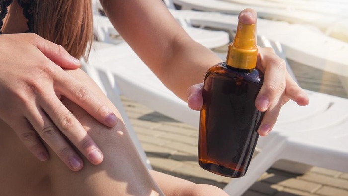 1236468852 Lady is massaging sunscreen lotion while sunbathing. Female model during summer vacation. Sunscreen suntan lotion in spray bottle. Young woman in spraying tanning oil on her leg from bottle in hand.