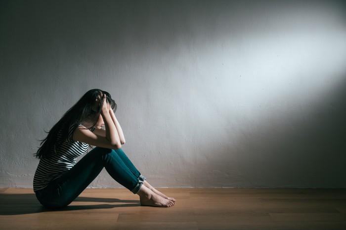 Anxiety disorder menopause woman, stressful depressed, panic attack person with mental health illness, headache and migraine sitting with back against wall on the floor in domestic home