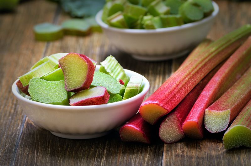 Fresh rhubarb in white bowl on wooden table