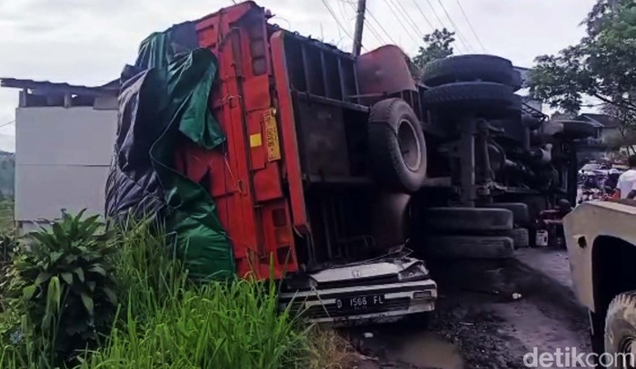 Truk pengangkut air minuman dalam kemasan terguling menimpa mobil di Jalan Raya Bogor - Sukabumi. Mobil yang tengah diparkir itu pun ringsek.