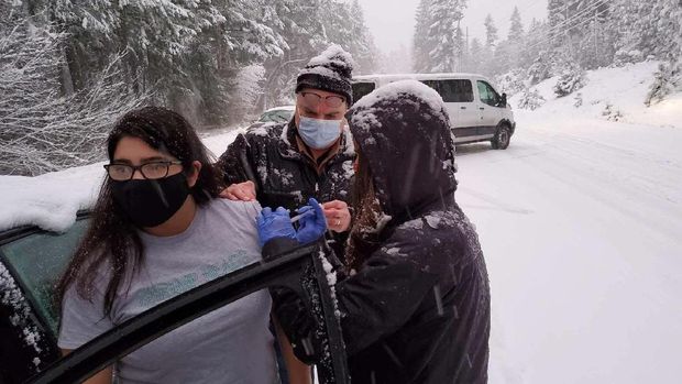 This photo provided by Josephine County, Ore., Public Health shows Josephine County Sheriff's Deputy Nicole Letona, left, receiving a COVID-19 vaccine administered by Dr. David Candelaria, center, and Leah Swanson, right, Josephine County Emergency Preparedness Coordinator, on Highway 199 near Hayes Hill, Ore., Thursday, Jan. 28, 2021, near Grants Pass. Oregon health workers who got stuck in the snowstorm on their way back from a COVID-19 vaccination event went car to car injecting stranded drivers before several of the doses expired. (Josephine County Public Health via AP)
