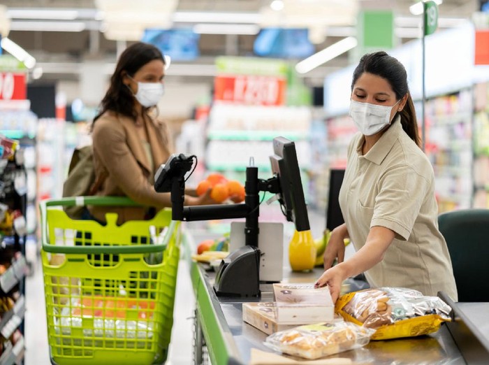 1225040489 Latin American cashier scanning products at a grocery store wearing a facemask - quarantine lifestyle concepts