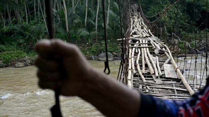JEMBATAN RAWAYAN RUSAK DI GARUT Warga memegang kawat penyanggah saat melintasi jembatan rawayan yang rusak di Desa Simpang, Cibalong, Kabupaten Garut, Jawa Barat, Minggu (31/1/2021). Jembatan penghubung antara Kabupaten Garut dan Kabupaten Tasikmalaya tersebut rusak akibat faktor usia sehingga menghambat aktivitas warga untuk akses mendapatkan fasilitas kesehatan, pendidikan, dan menjual hasil bumi. ANTARA FOTO/Candra Yanuarsyah/agr/hp.