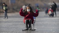Seorang gadis berseluncur menggunakan kursi di permukaan kanal yang membeku di Beijing, China.  
