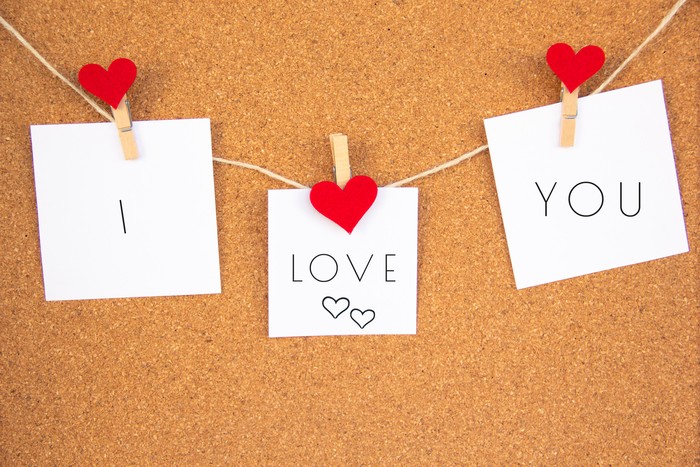 i love you lettering with hearts on 3 white paper pinned with 2 small red heart pegs and one big red heart pegs on cork board