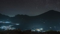 Langit bertabur bintang menghiasi pemandangan gemerlap cahaya lampu desa Sembalun dan siluet gunung Rinjani.