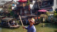 Salah seorang pengemudi kapal mendayung dan mengarahkan perahu di kanal