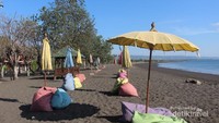 Pemandangan pantai bagi pengunjung wanita dengan bangku dan payung warna warni.