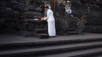 Seorang ibu sedang menaruh sesajen di gerbang Pura.