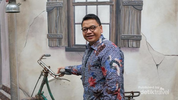 Pengunjung yang berfoto dengan sepeda onthel tua dengan mural yang menarik