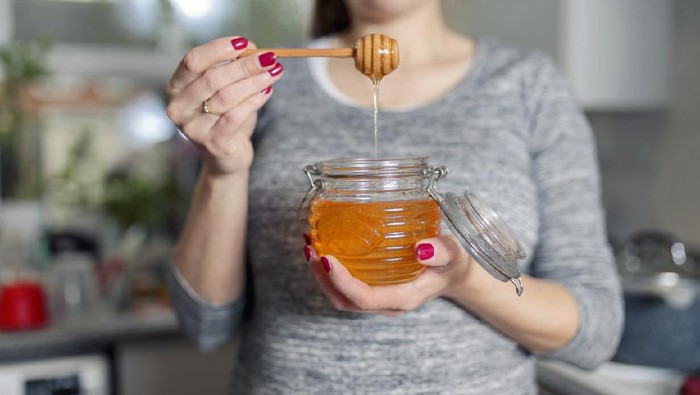 Ilustrasi makan madu Woman holding jar of honey in kitchen