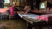 Warga menyaksikan tayangan televisi di dalam rumahnya yang terendam banjir di Desa Sayung, Kecamatan Sayung, Kabupaten Demak, Jawa Tengah, Minggu (7/2/2021). Berdasarkan data dari Kantor Balai Desa Sayung, sebanyak 3.161 keluarga dengan total 10.297 jiwa yang tersebar di delapan dukuh di desa tersebut terendam banjir dengan variasi ketinggian sekitar 40-120 cm disebabkan oleh curah hujan tinggi serta meluapnya Sungai Dombo Sayung. ANTARA FOTO/Aji Styawan
