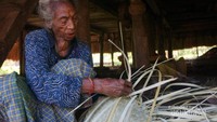 Seorang nenek sedang membuat peralatan dapur dengan anyaman daun lontar