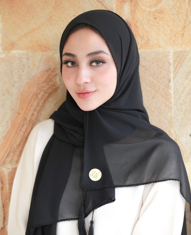 Wanita yang lahir pada 8 Juli 2000 ini, tampak seperti wanita Timur Tengah ketika memakai hijab pashmina warna hitam. Detail ujung hijab terdapat tasel dan juga logo plat gold. Foto: Dok. Instagram @mwbymargin_catalog.