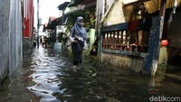 Seorang warga tampak melintasi jalan yang terendam banjir untuk berangkat kerja.