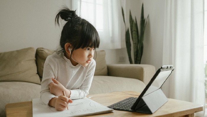 Young woman wearing headphones learning using digital tablet and teleconferencing apps in living room at home