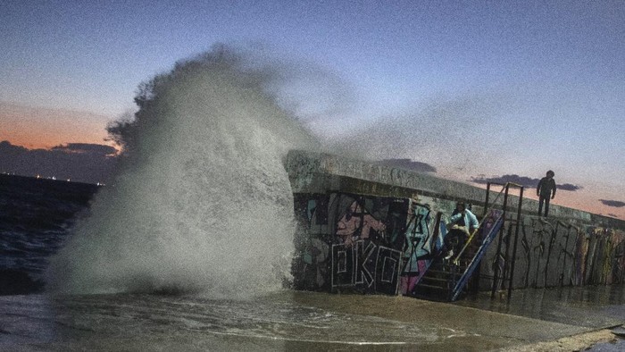 Gelombang Besar Hantam Pantai Yunani A young women goes down the stairs as a wave hits a wave-lashed breakwater during a windy afternoon in the southern Athens coastal suburb of Flisvos, on Monday, Feb. 8, 2021. A cold and strong winter weather hit Europe with temperatures far below zero. (AP Photo/Petros Giannakouris)