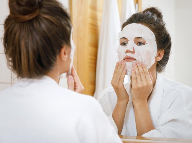 Woman is applying sheet mask on her face in the bathroom