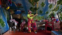 Mengenakan jumpsuit polkadot merah, dengan riasan mencolok dan coretan cat putih di wajahnya, para pemain sirkus siap memulai pertunjukan.  