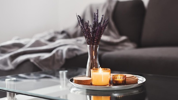 Coffee table design idea: aroma candles and dried lavender bouquet on a metal tray, sofa with grey blanket on background. Simple Scandinavian home decor. Hygge concept