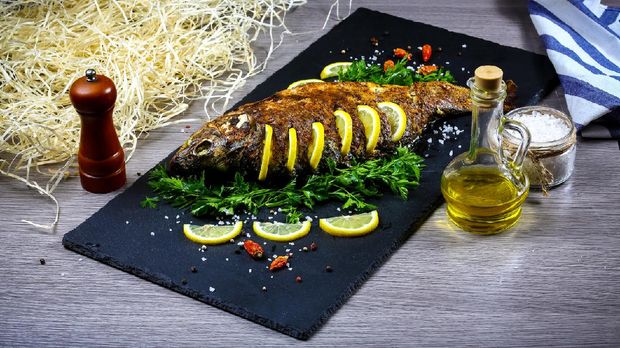 Grilled river fish on a plate with lemon and baked vegetables and parsley. Food recipe photo, copy text.