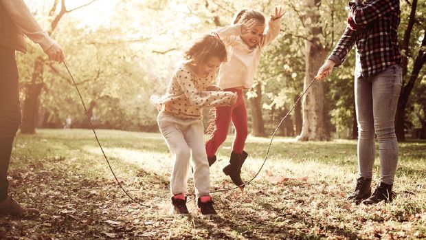 Cheerful family playing with jump rope together in park.
