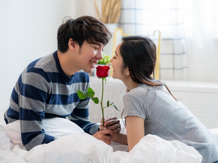 Ilustrasi Hari Valentine Romantic Asian couple in the bedroom, a man giving a rose to a beautiful woman and both kissing a beautiful rose with love and happiness, Beautiful elegant Asian couple is hugging and smiling in bedroom