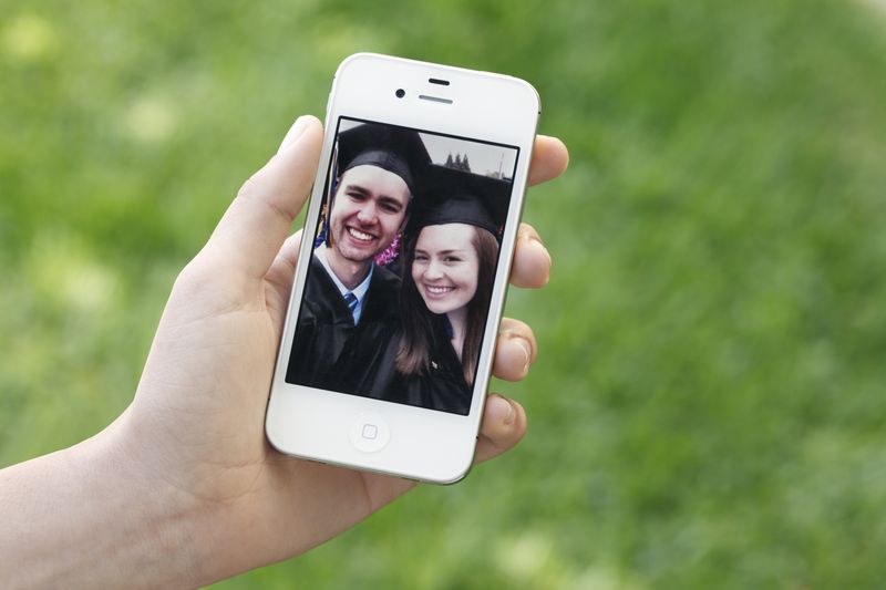 San Diego, California, USA - May 25, 2011:  A young woman holding a white Apple iPhone 4.  An image of a couple of college graduates appears on the screen.