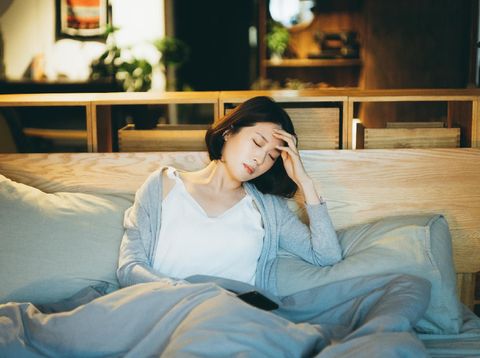 Young Asian woman feeling sick and suffering from a headache, lying on the bed and taking a rest at home