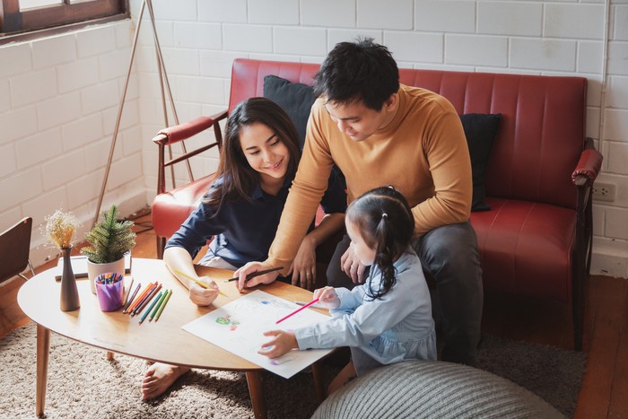 Family at home playing and teaching child girl how to draw.