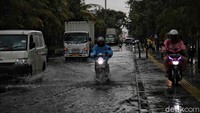 Pemotor melintas di trotoar untuk menghindari genangan.