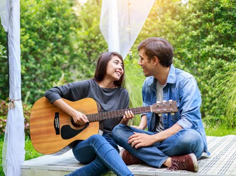 Young Asian loving couple playing guitar in the park, outdoors