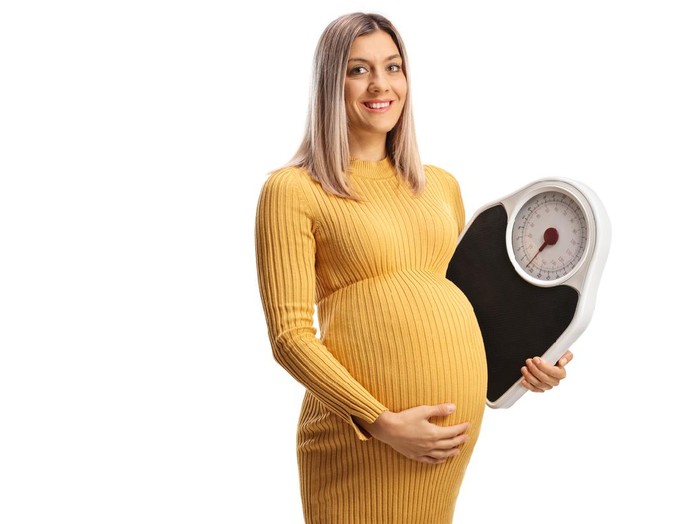 Berat badan ibu hamil Pregnant woman smiling and holding a weight scale isolated on white background