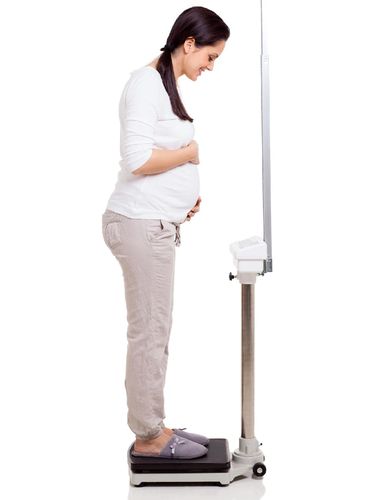 Pregnant woman smiling and holding a weight scale isolated on white background