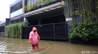 Seorang warga melintas di jalanan yang terendam banjir setinggi lutut di Perumahan Jatibening Permai.