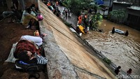 Warga mengungsi sambil terus memantau banjir yang merendam rumahnya.