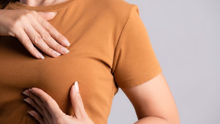 Ilustrasi Kanker Payudara Woman hand checking lumps on her breast for signs of breast cancer on gray background. Healthcare concept.