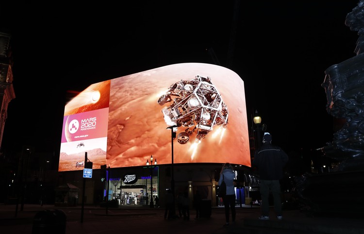Images from Nasa are streamed live showing the landing of NASAs Perseverance on Mars, shown on Piccadilly Lights in central London, Thursday Feb. 18, 2021.  The Mars rover landing mission begins its search for traces of life after the successful landing, to explore and collect samples for future return to Earth. Eros statue top left. (AP Photo/Alastair Grant)