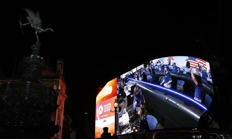 Images from Nasa are streamed live showing the landing of NASAs Perseverance on Mars, shown on Piccadilly Lights in central London, Thursday Feb. 18, 2021.  The Mars rover landing mission begins its search for traces of life after the successful landing, to explore and collect samples for future return to Earth. Eros statue top left. (AP Photo/Alastair Grant)