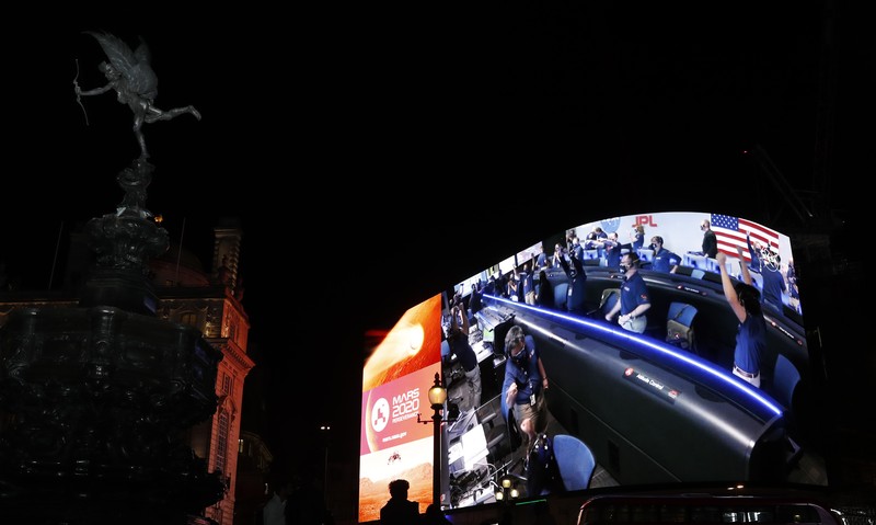 Images from Nasa are streamed live showing the landing of NASA's Perseverance on Mars, shown on Piccadilly Lights in central London, Thursday Feb. 18, 2021. The Mars rover landing mission begins it's search for traces of life after the successful landing, to explore and collect samples for future return to Earth. Eros statue top left. (AP Photo/Alastair Grant)