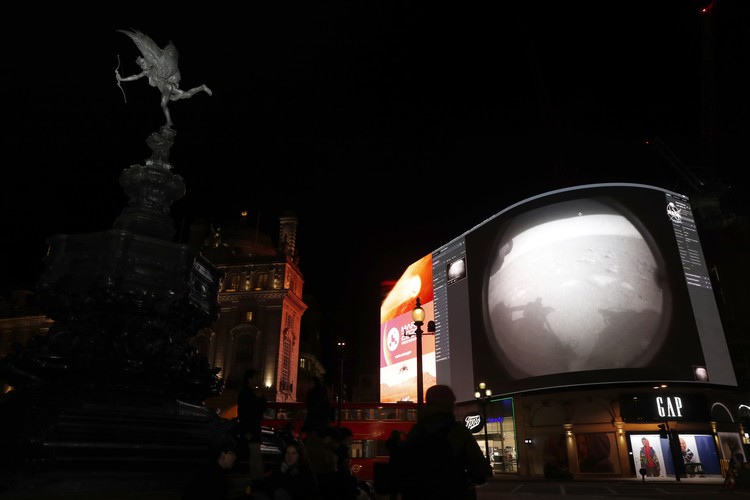 Images from Nasa are streamed live showing the landing of NASAs Perseverance on Mars, shown on Piccadilly Lights in central London, Thursday Feb. 18, 2021.  The Mars rover landing mission begins its search for traces of life after the successful landing, to explore and collect samples for future return to Earth. Eros statue top left. (AP Photo/Alastair Grant)
