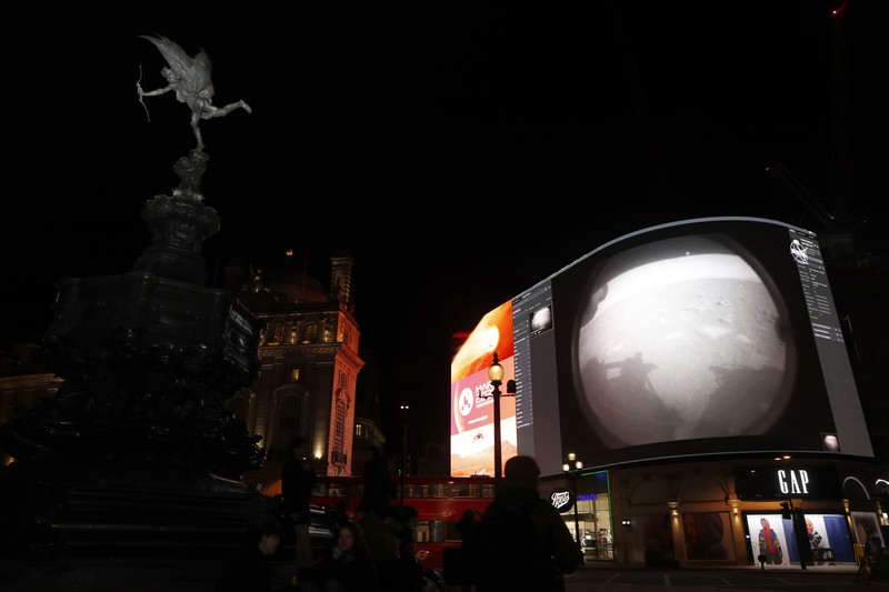 Images from Nasa are streamed live showing the landing of NASA's Perseverance on Mars, shown on Piccadilly Lights in central London, Thursday Feb. 18, 2021. The Mars rover landing mission begins it's search for traces of life after the successful landing, to explore and collect samples for future return to Earth. Eros statue top left. (AP Photo/Alastair Grant)