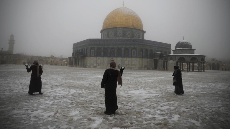 Yerusalem Diselumuti Salju Wanita bermain di Kubah Batu di komplek Masjid Al Aqsa yang diselumuti salju, Kamis Feb. 18, 2021. (AP Photo/Mahmoud Illean)