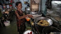 Seorang warga memasak di dalam dapur yang tergenang banjir.