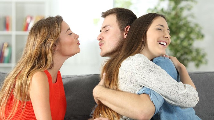 Boy cheating to his girlfriend with her best friend sitting on a couch at home