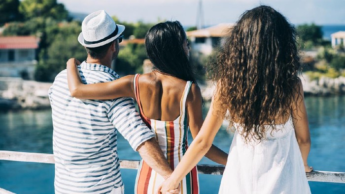 Couple in vacations standing on harbor, man hoding other womans hand.