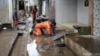Seorang petugas membersihkan saluran air di depan rumah warga dari sampah.