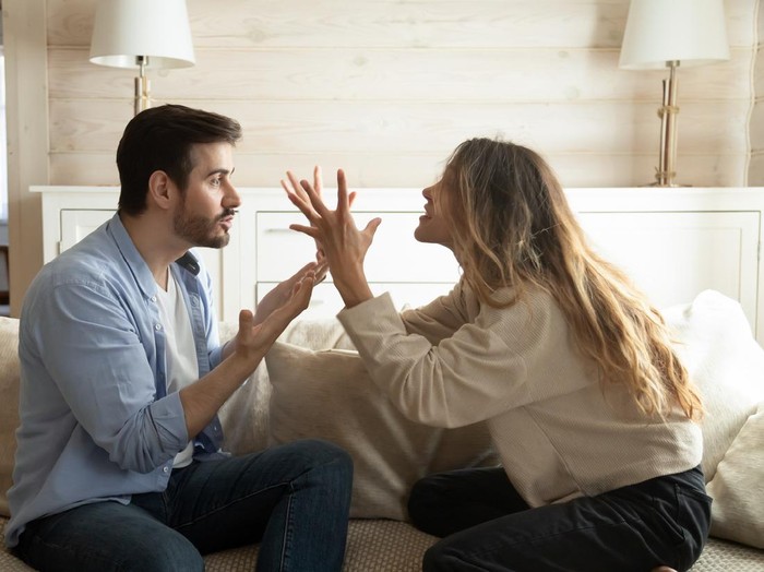 Emotional annoyed stressed couple sitting on couch, arguing at home. Angry irritated nervous woman man shouting at each other, figuring out relations, feeling outraged, relationship problems concept.