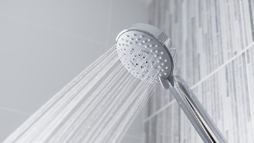 Fresh shower behind wet glass window with water drops splashing. Water running from shower head and faucet in modern bathroom.
