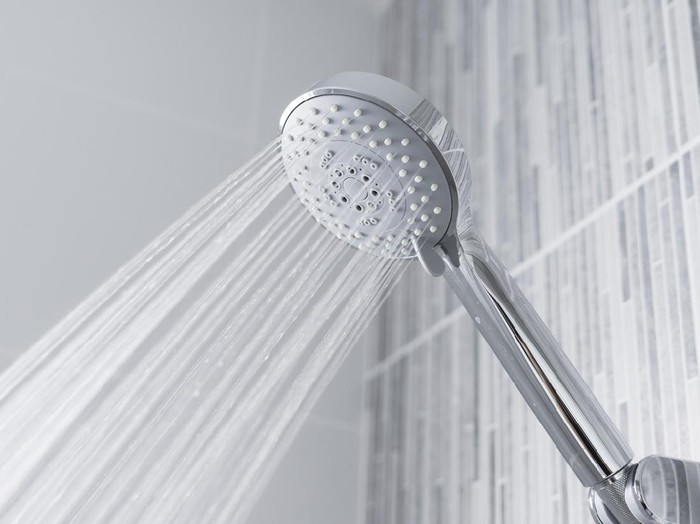 Fresh shower behind wet glass window with water drops splashing. Water running from shower head and faucet in modern bathroom.